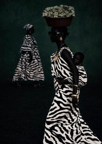 Woman in zebra-striped dress carrying a child and basket on her head against a dark background